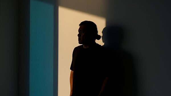 Eine nachdenklich wirkende Person steht im Schatten an einer Wand, mit Blick in Richtung Licht – Symbolbild für psychische Belastung und Hoffnung auf Veränderung bei Glücksspielsucht.