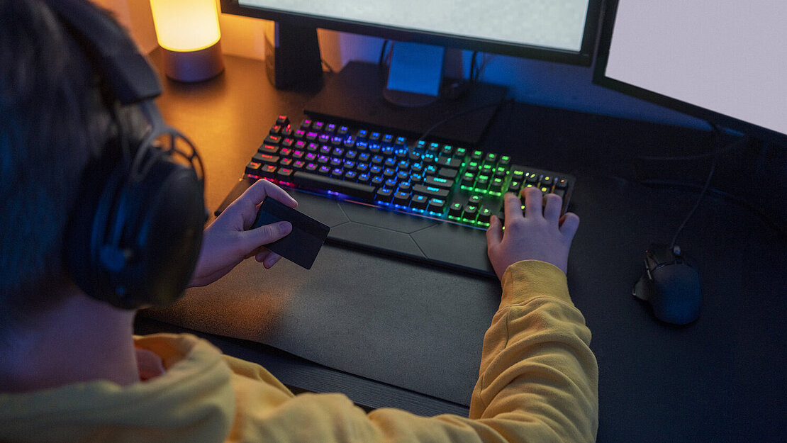Gamer sitzt am PC und hält eine Kreditkarte in der Hand – Symbol für Gamblification und den Einfluss von Glücksspielelementen in Videospielen.